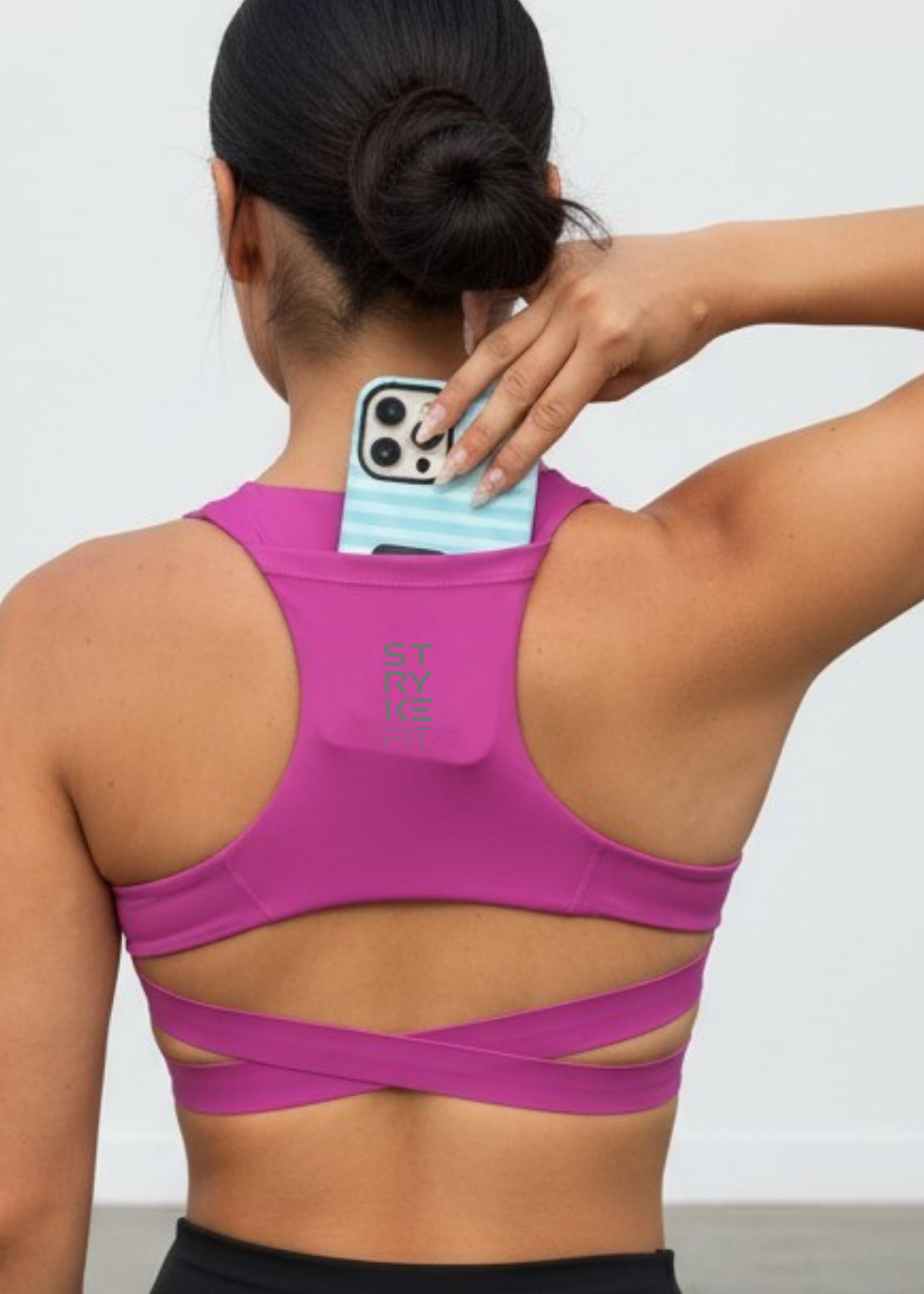 A woman shown from behind wearing a bright pink sports bra with crisscross back straps and a light blue striped phone case inserted into the back pocket. The brand name 'ST FRY' is printed vertically on the back of the bra.