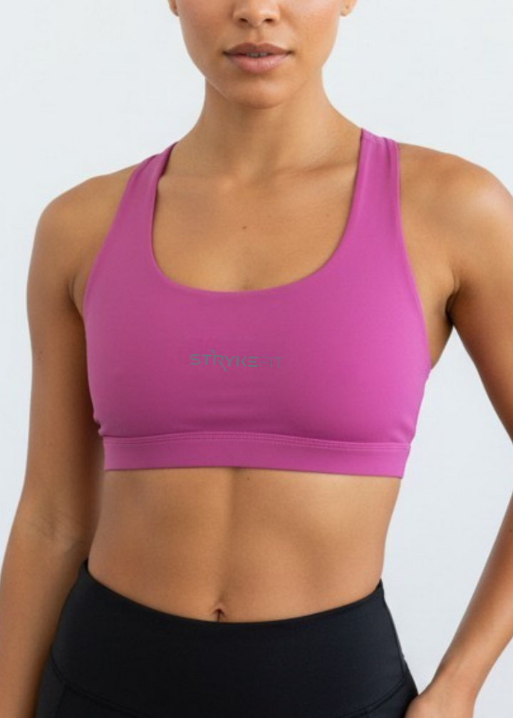 A woman modeling a bright pink athletic sports bra with a scoop neckline and wide shoulder straps, paired with black high-waisted leggings, against a plain white studio background.