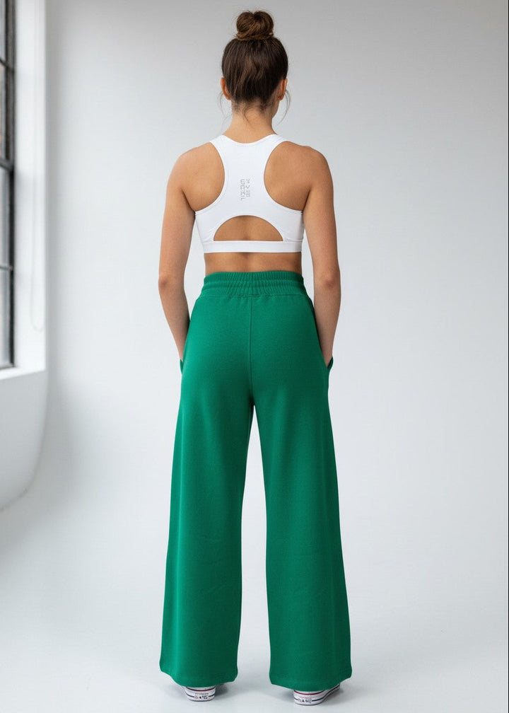 Woman wearing a white sports bra and green high-waisted pants in a minimalistic setting. Our ACTIVE FLEECE TRACKPANTS is the perfect staple piece for your pre and post-training session.
These trackpants are a relaxed high waist fit with a rib elasticated waistband, drawstring, side pockets, and beautiful, soft brushed fleece fabric.

DETAILS, Premium brushed fleece, Rib waistband with drawstring, Side pockets, Printed logo on left leg