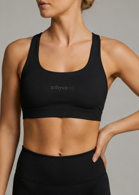 A woman modeling a black athletic sports bra and matching high-waisted shorts against a solid gray studio background. The brand name 'STRYKE FIT' is printed in reflective on the center of the sports bra. The ATHLETE CROP TOP features a discrete back pocket, keeping your essentials close, whether it's your phone, gels, keys, or anything you need to go the distance without distractions.

The performance racerback design follows the natural line of your shoulders, allowing unrestricted movement
