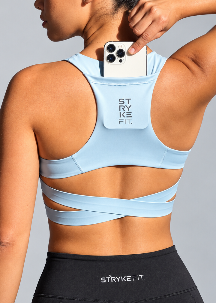 A woman shown from the back wearing a light blue sports bra with a phone pocket on the upper back, holding a white smartphone inside the pocket. She is also wearing black athletic shorts with the brand name 'STRYKEFIT' visible on the waistband. The ATHLETE CROP TOP features a discrete back pocket, keeping your essentials close, whether it's your phone, gels, keys, or anything you need to go the distance without distractions.

The performance racerback design follows the natural line of your shoulders, allow