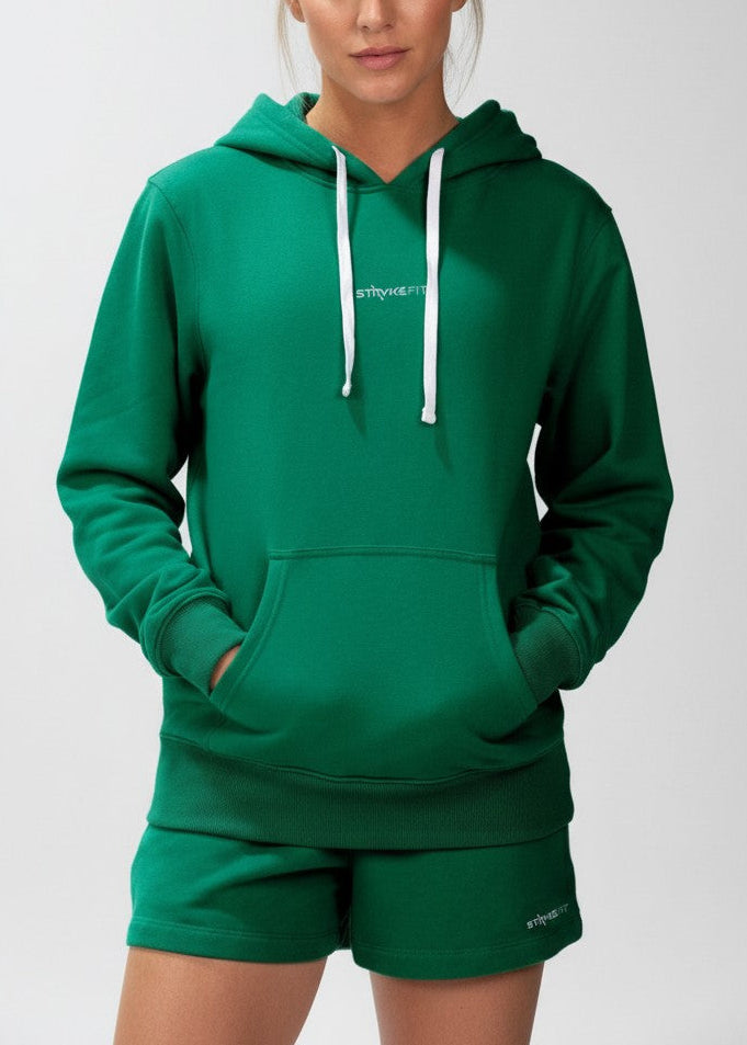 Woman wearing a green hoodie and shorts set on a white background. The Core Hooded Fleece is designed for everyday wear, combining comfort with effortless style. Made from premium brushed-back fleece, it delivers a soft, warm feel while remaining easy to wear and versatile. DETAILS, Premium brushed fleece, Self-lined hood, Kangaroo pocket, Soft ribbed cuffs, Printed logo