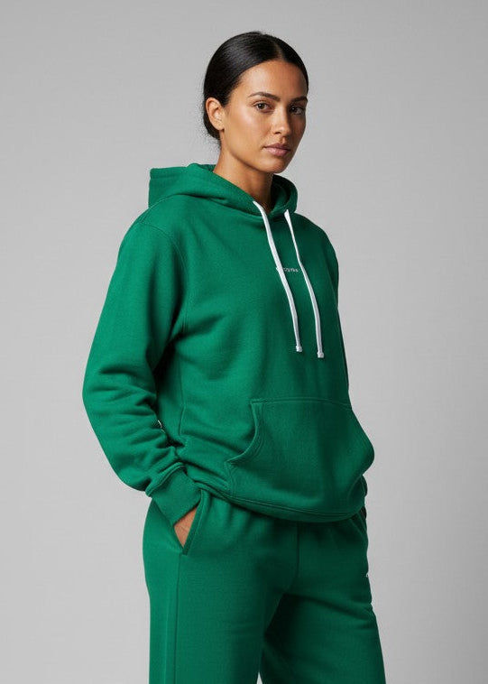 Woman wearing a green hoodie and shorts set on a white background. The Core Hooded Fleece is designed for everyday wear, combining comfort with effortless style. Made from premium brushed-back fleece, it delivers a soft, warm feel while remaining easy to wear and versatile. DETAILS, Premium brushed fleece, Self-lined hood, Kangaroo pocket, Soft ribbed cuffs, Printed logo