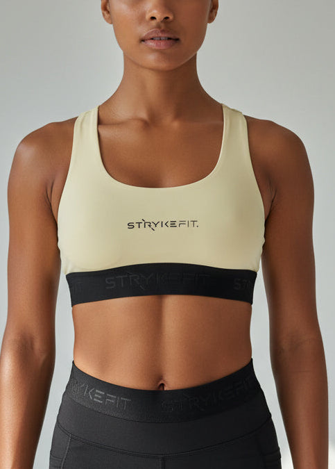 Woman wearing a beige sports bra and black shorts with 'STUDIOFIT' branding on a neutral background. The FIT 2.0 CROP TOP is a new version of our most popular style, this crop has a discreet back pocket to stash your phone, gels, or any running essentials.&nbsp;

The racerback design follows the natural line of your shoulders, unlocking full arm mobility while delivering uncompromising support. Lightweight, breathable, and made to move with you from the first step to the final sprint.
