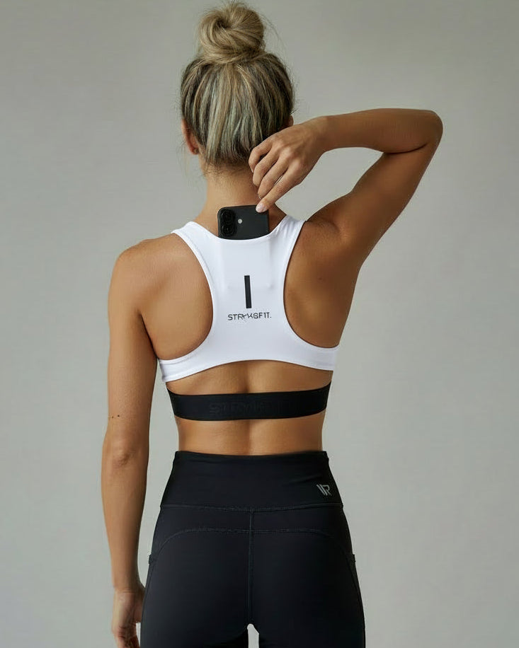 Person wearing a white sports bra with a black band and black leggings on a plain background. The FIT 2.0 CROP TOP is a new version of our most popular style, this crop has a discreet back pocket to stash your phone, gels, or any running essentials.&nbsp;

The racerback design follows the natural line of your shoulders, unlocking full arm mobility while delivering uncompromising support. Lightweight, breathable, and made to move with you from the first step to the final sprint.