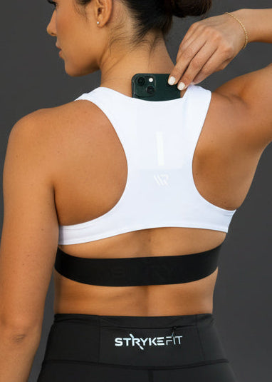 Woman wearing a white sports bra and black shorts with 'STRIVE FIT' branding on a dark background. The FIT 2.0 CROP TOP is a new version of our most popular style, this crop has a discreet back pocket to stash your phone, gels, or any running essentials.&nbsp;

The racerback design follows the natural line of your shoulders, unlocking full arm mobility while delivering uncompromising support. Lightweight, breathable, and made to move wi